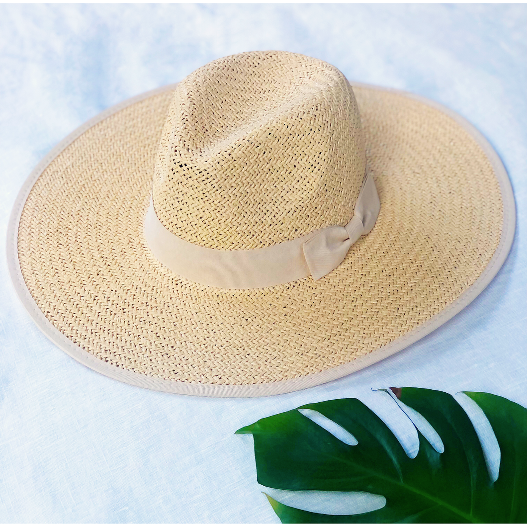 wide brim fedora straw hat with cream ribbon next to monstera leaf